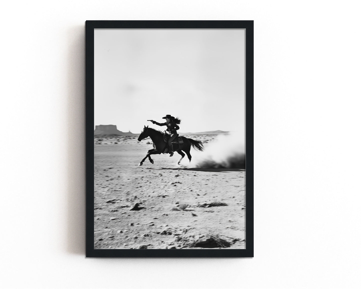 A black-and-white photograph of a cowboy galloping on horseback through the desert, with dramatic light and shadow across the sand.