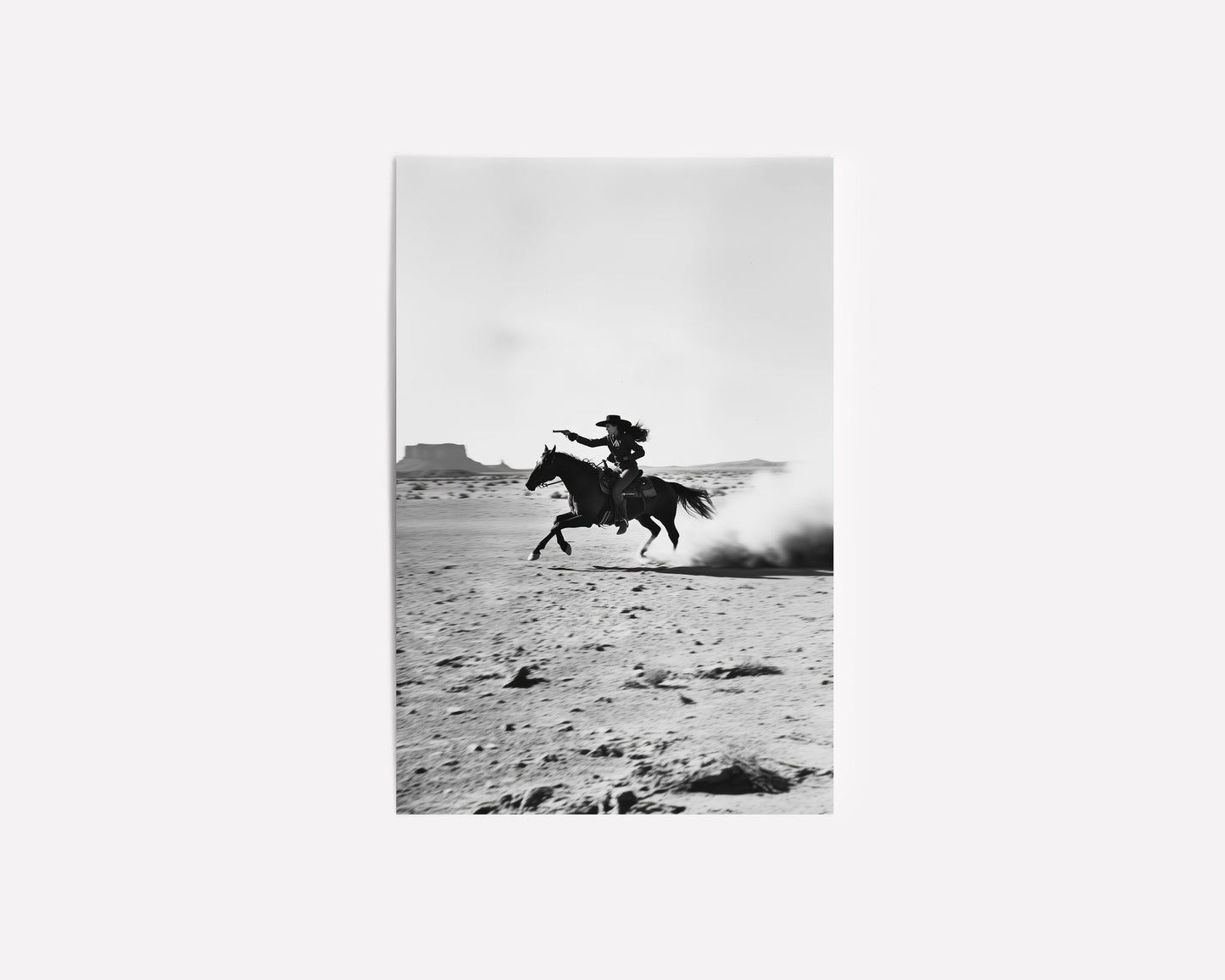 A black-and-white photograph of a cowboy galloping on horseback through the desert, with dramatic light and shadow across the sand.