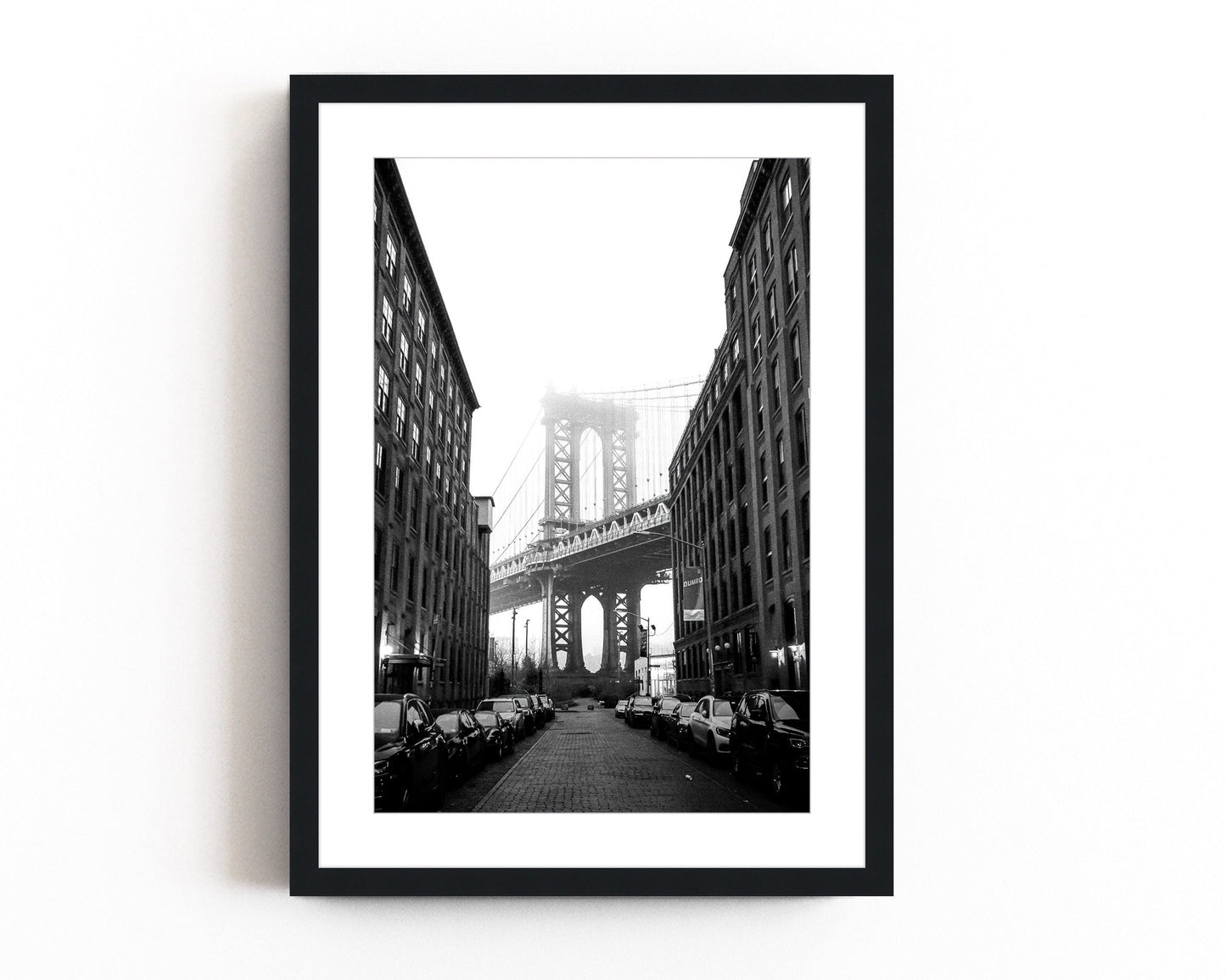 Black and white photography of the Manhattan Bridge framed between two buildings in DUMBO, Brooklyn, capturing the timeless beauty of NYC architecture.
