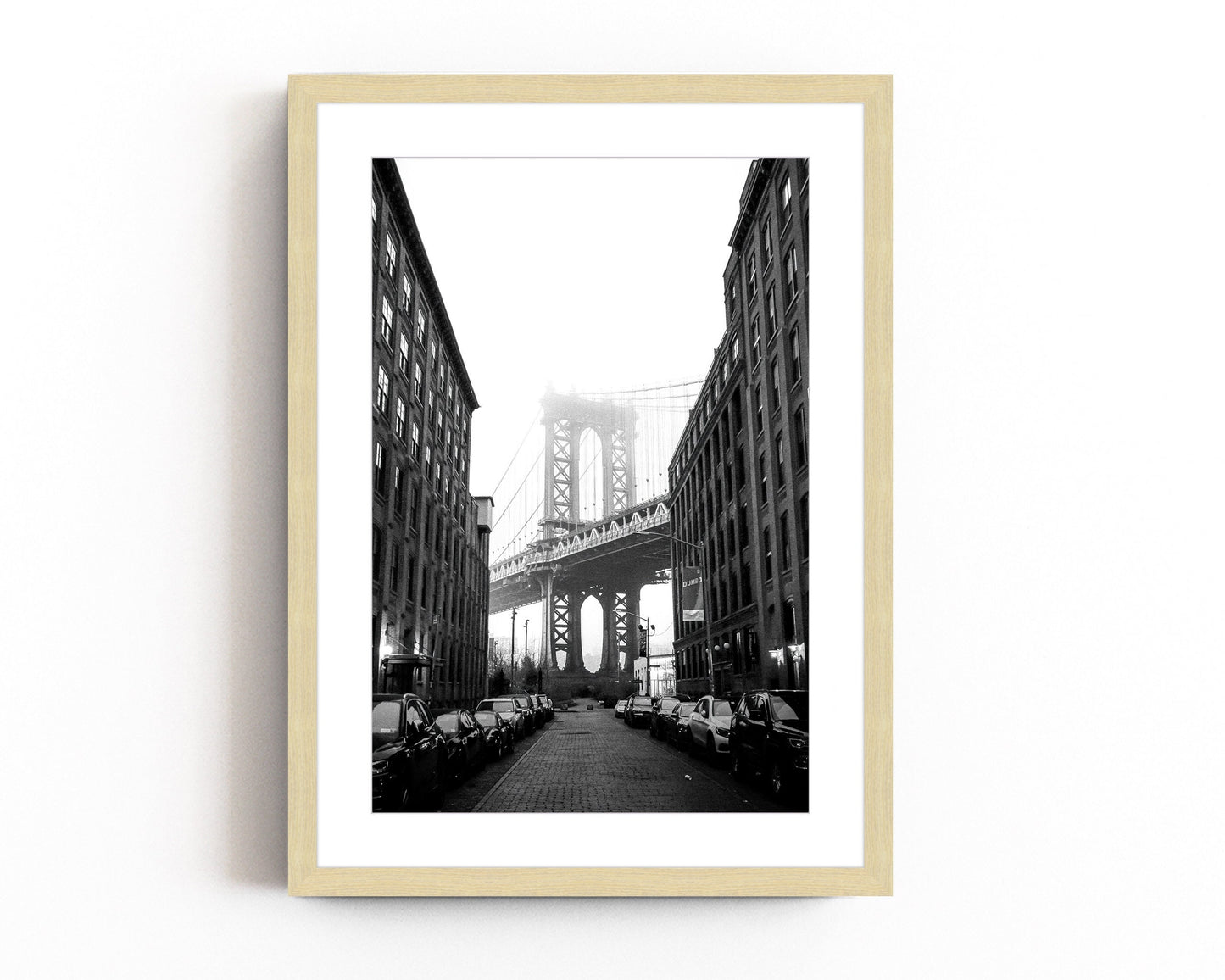 Black and white photography of the Manhattan Bridge framed between two buildings in DUMBO, Brooklyn, capturing the timeless beauty of NYC architecture.