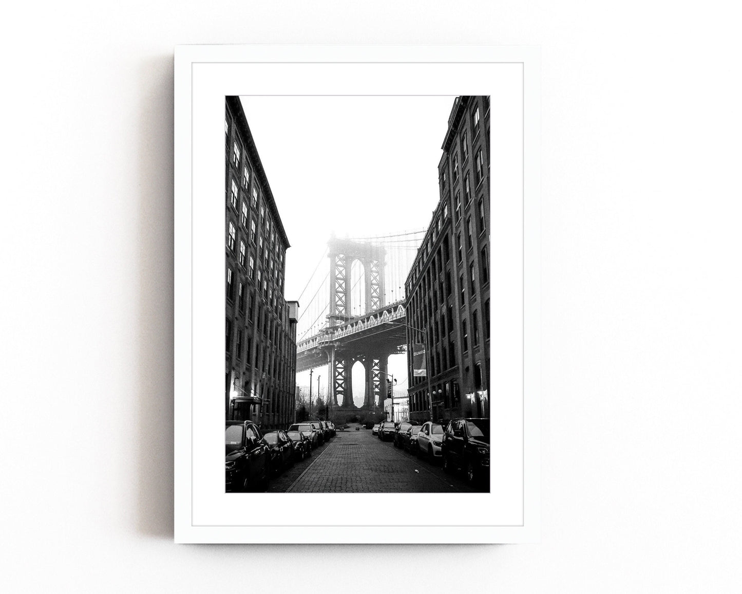 Black and white photography of the Manhattan Bridge framed between two buildings in DUMBO, Brooklyn, capturing the timeless beauty of NYC architecture.