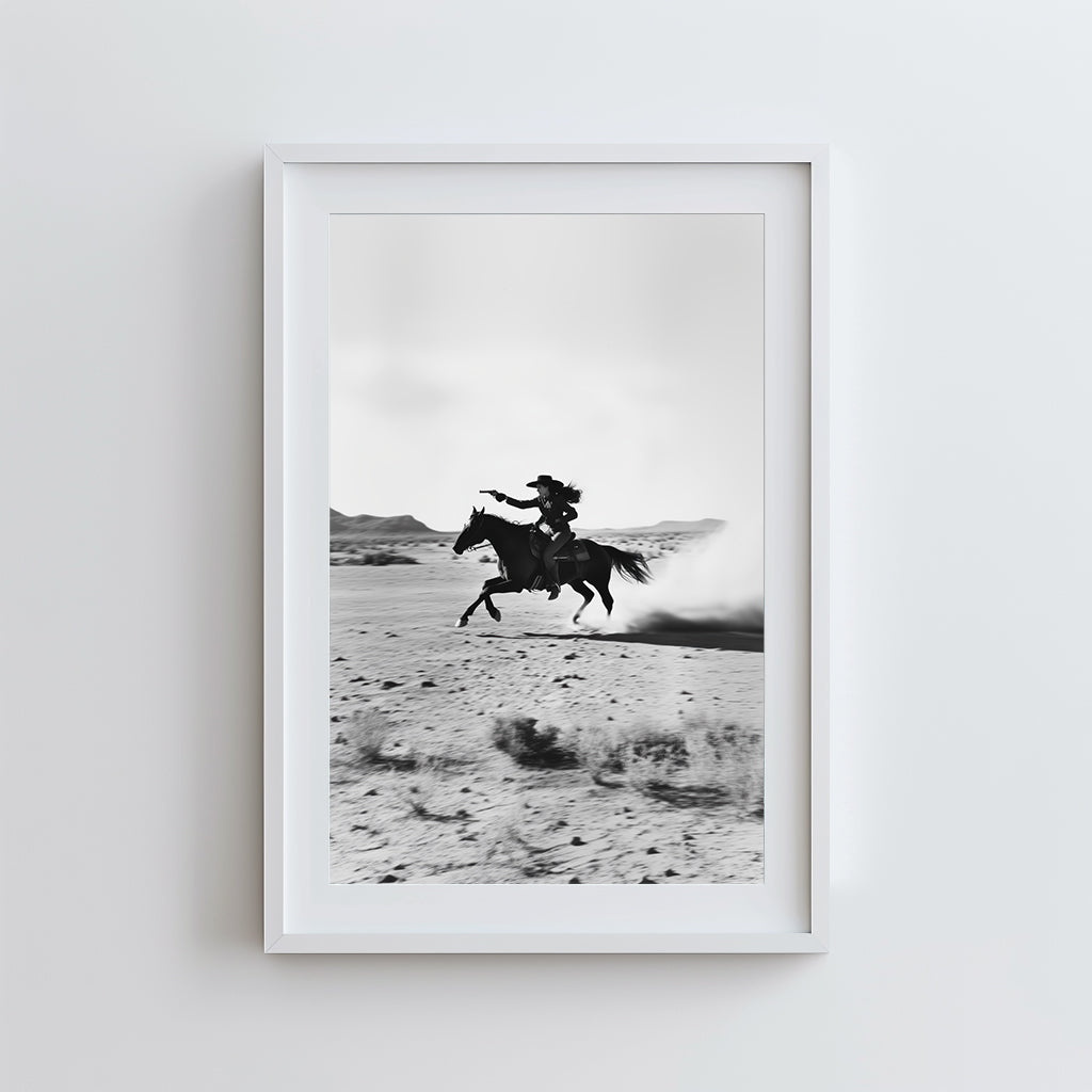A black-and-white photograph of a cowboy galloping on horseback through the desert, with dramatic light and shadow across the sand.