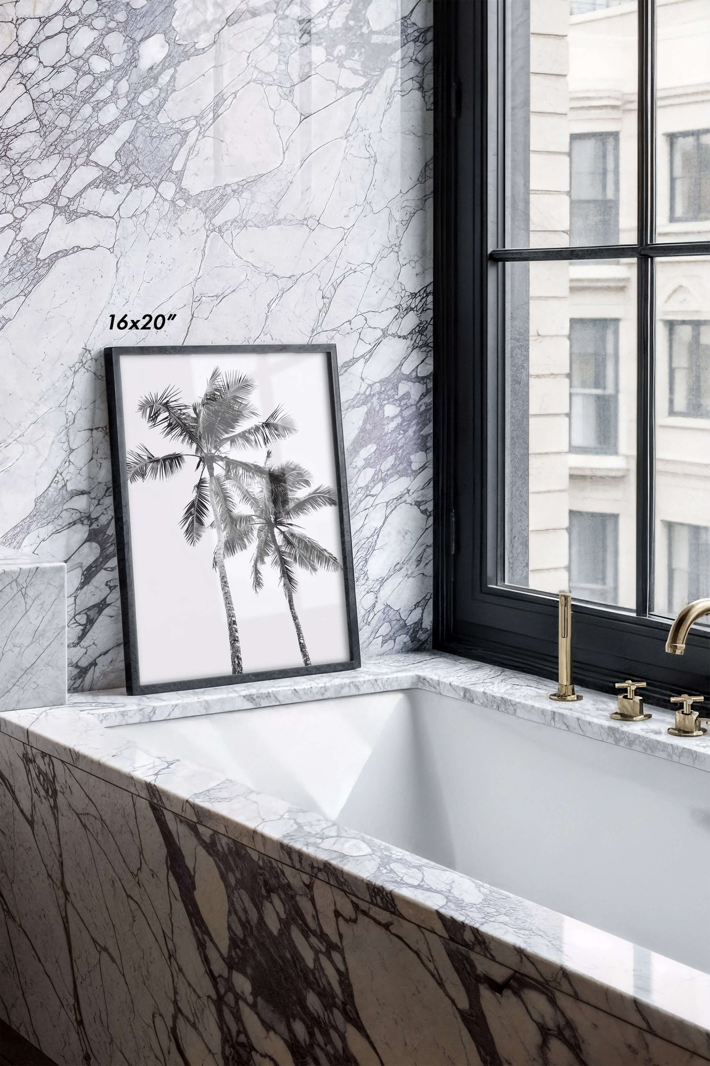 A framed black and white palm tree wall art print leaning against a marble-patterned bathroom wall next to a window with a black frame. The print has a small '16x20"' size overlay.