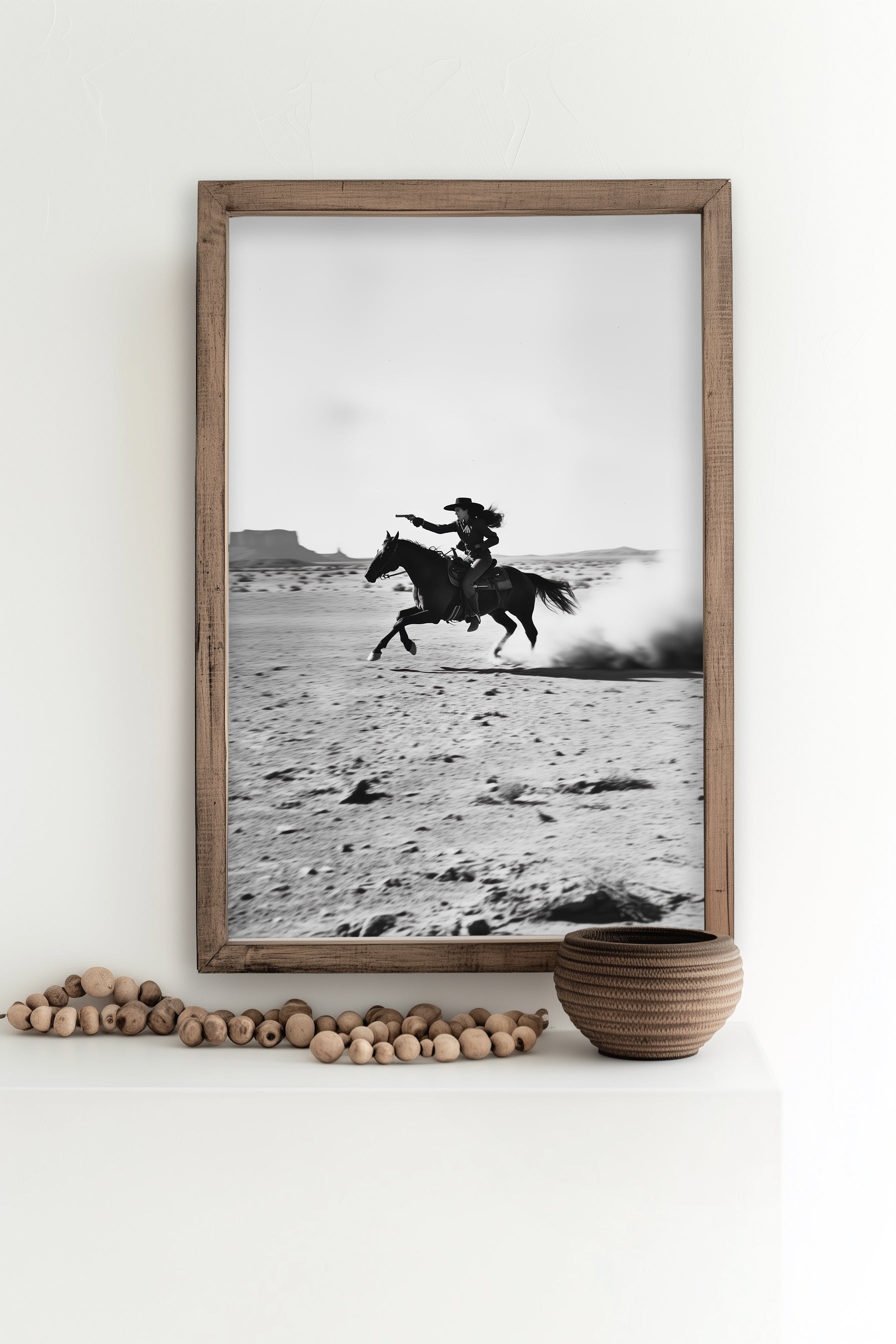 A black-and-white photograph of a cowboy galloping on horseback through the desert, with dramatic light and shadow across the sand.