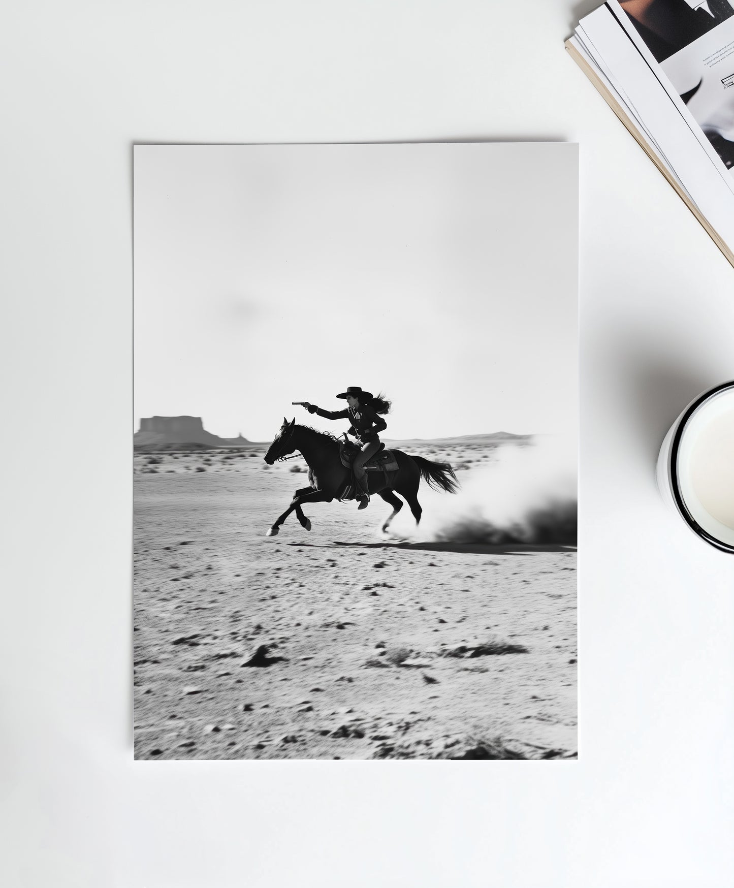 A black-and-white photograph of a cowboy galloping on horseback through the desert, with dramatic light and shadow across the sand.