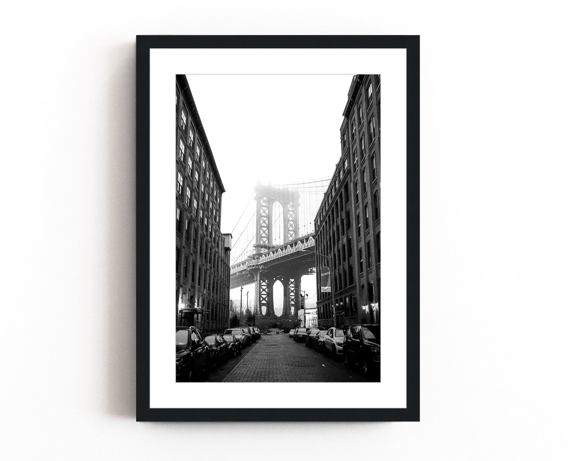  Black and white photography of the Manhattan Bridge framed between two buildings in DUMBO, Brooklyn, capturing the timeless beauty of NYC architecture.