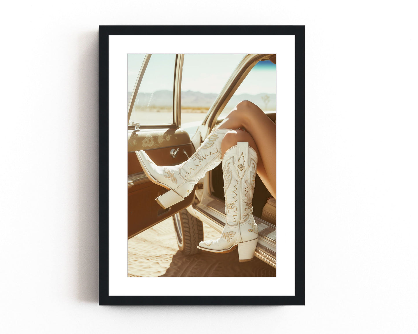 Western fashion photography print featuring white cowboy boots resting on the window of a vintage car, with a desert backdrop capturing a modern western style.