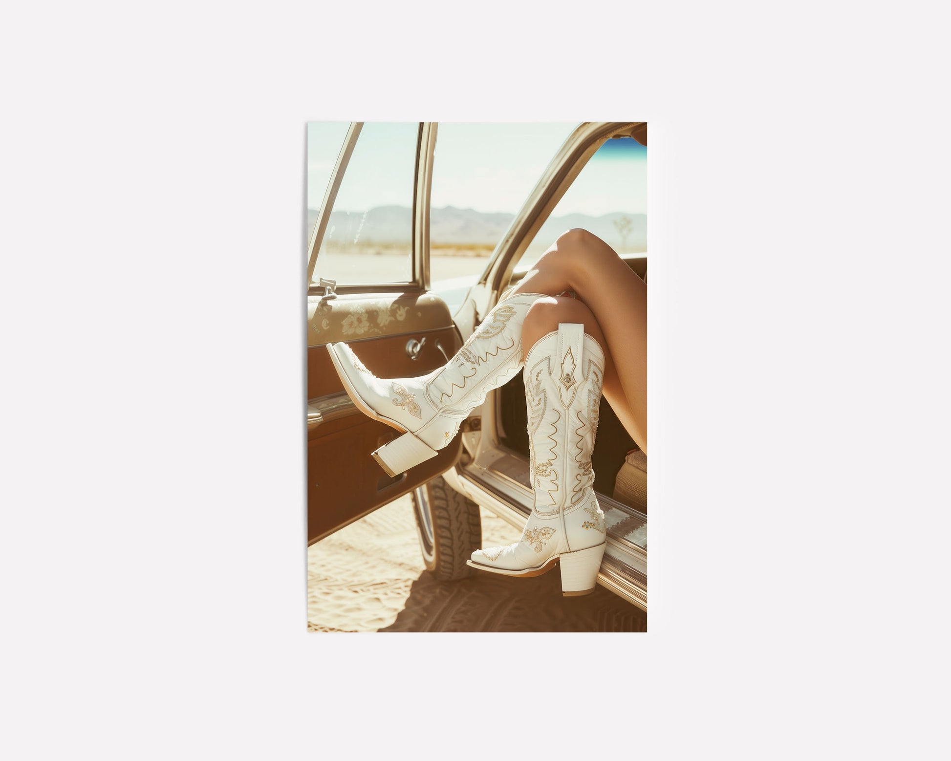 Western fashion photography print featuring white cowboy boots resting on the window of a vintage car, with a desert backdrop capturing a modern western style.