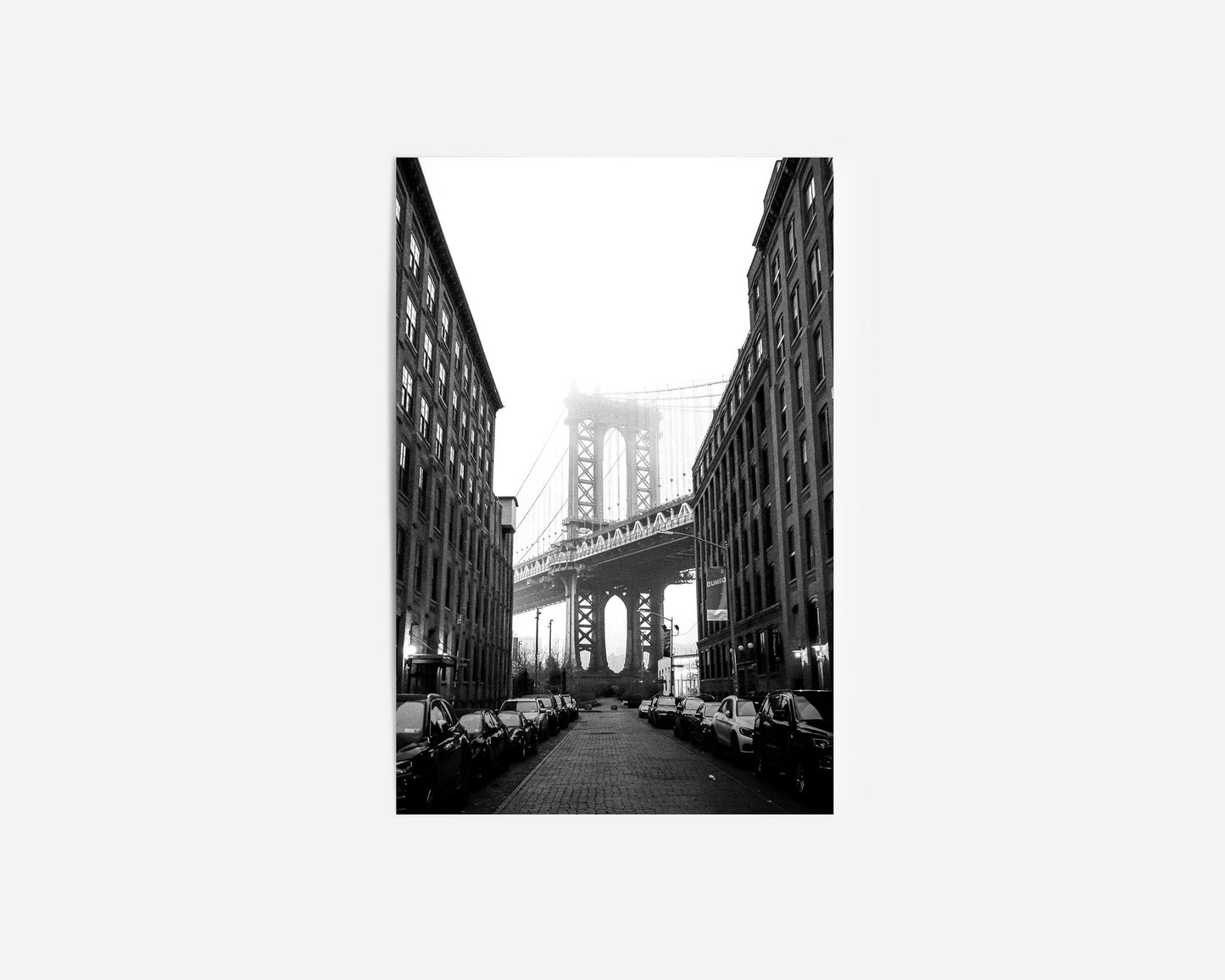  Black and white photography of the Manhattan Bridge framed between two buildings in DUMBO, Brooklyn, capturing the timeless beauty of NYC architecture.