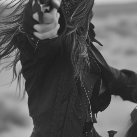 Black and white photograph of a female cowboy riding a horse, wearing a hat and bandana, aiming a revolver directly at the camera. The image captures a powerful, dramatic moment with a Western theme.