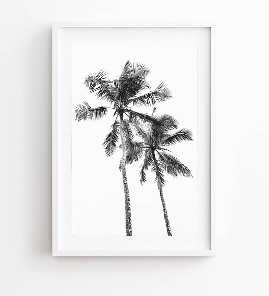 A minimalist black and white art print of two palm trees, presented in a clean white frame against a white wall.